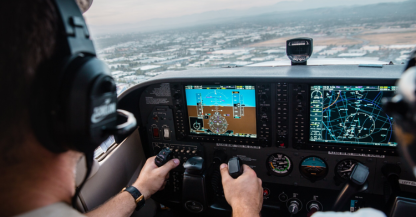Two pilots in the cockpit of a light aircraft with glass avionics displays, flying over a city